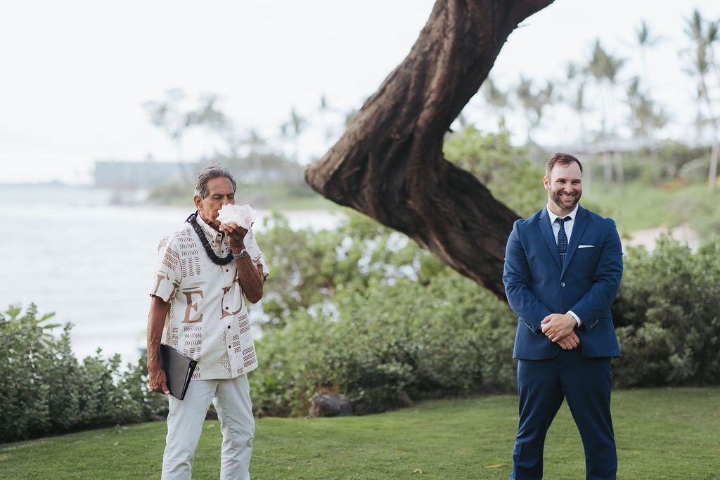 groom waiting on bride as officiant blows in shell for hawaiian wedding ceremony