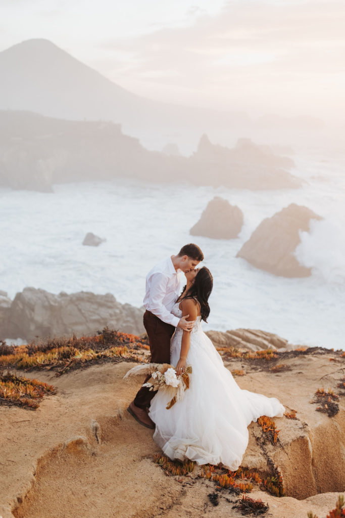 bride and groom portraits on rocky big sur coast with waves crashing behind them
