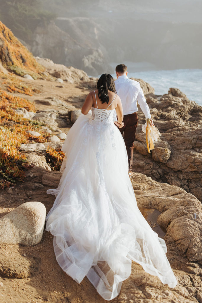 bride and groom walking on rocky coast in big sur
