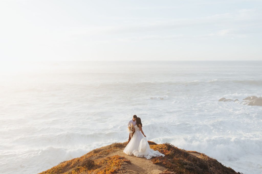 bride and groom portraits on the coast in big sur with waves crashing behind them