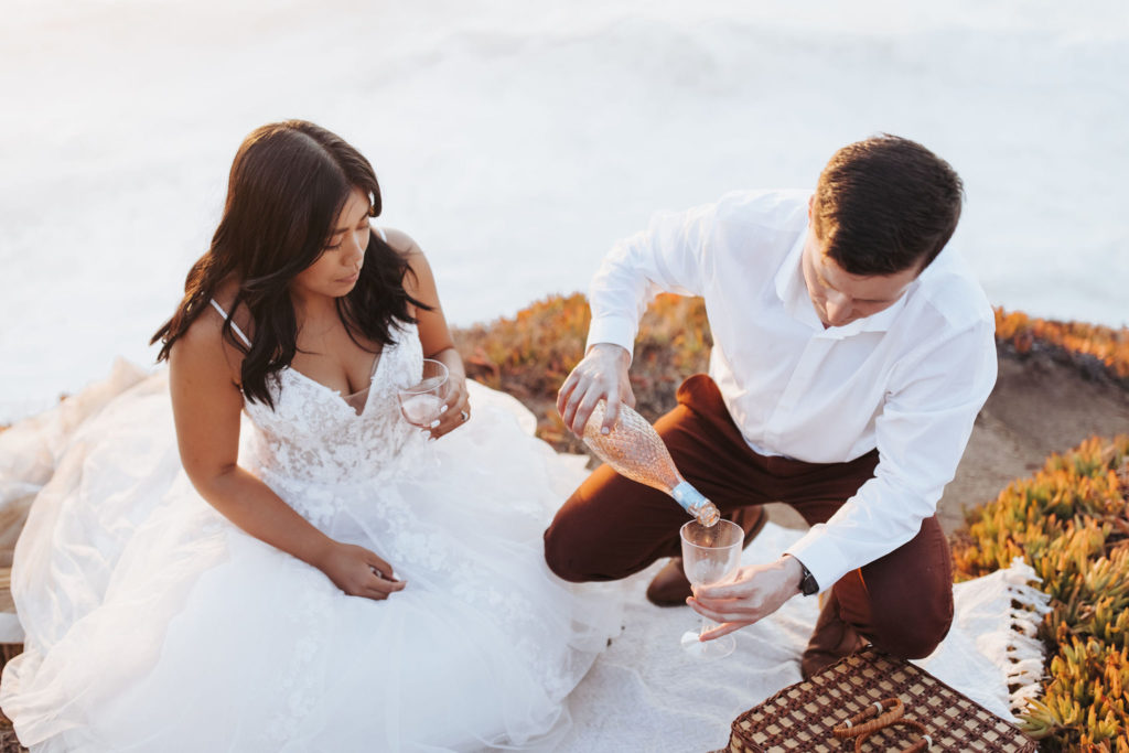 bride and groom pouring champagne at big sur elopement picnic