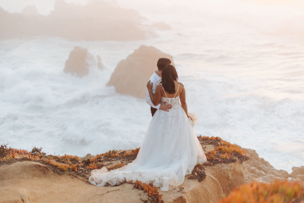 bride and groom portraits on rocky big sur coast with waves crashing behind them