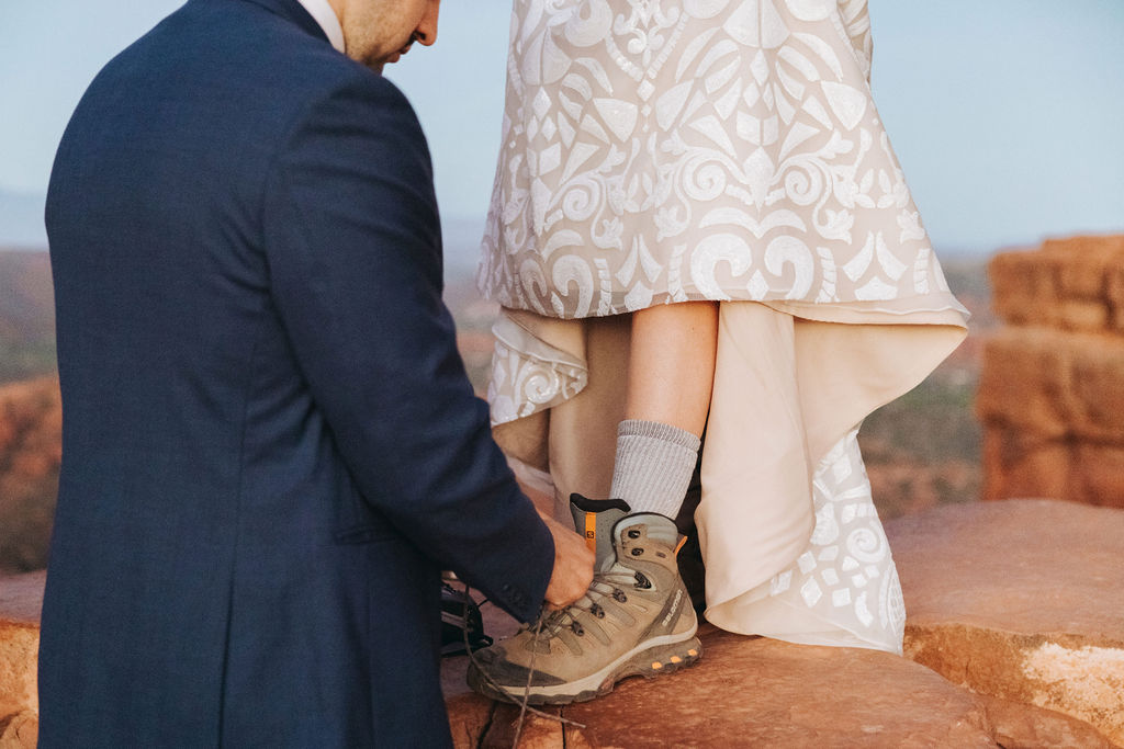 groom putting on bride's hiking shoes for cathedral rock elopement