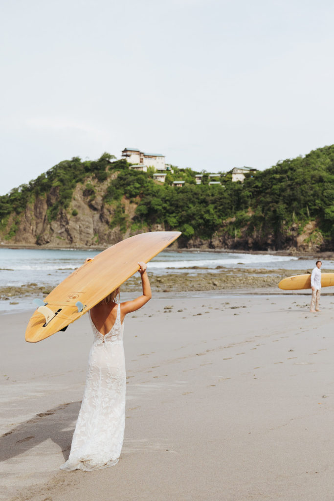 bride and groom holding surfboards on costa rica beach