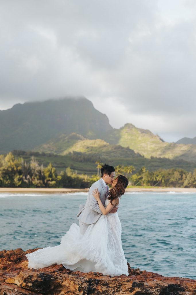 bride and groom standing on rocky cliff in kauai hawaii