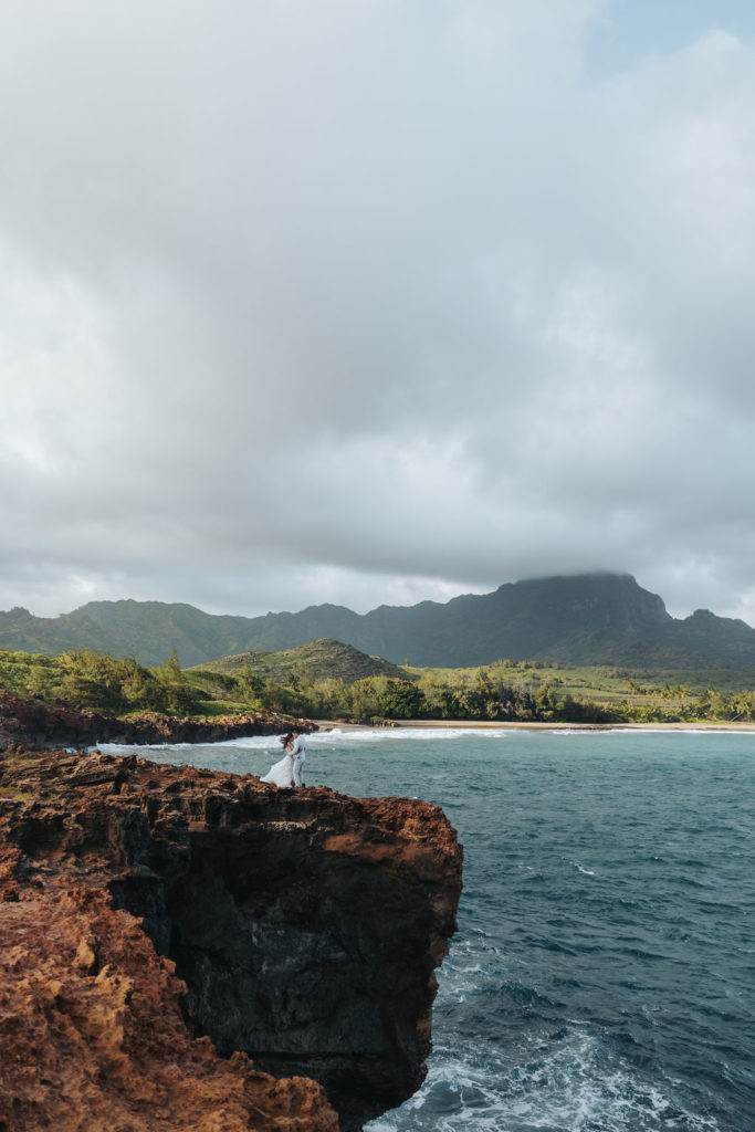 bride and groom standing on rocky cliff in kauai hawaii