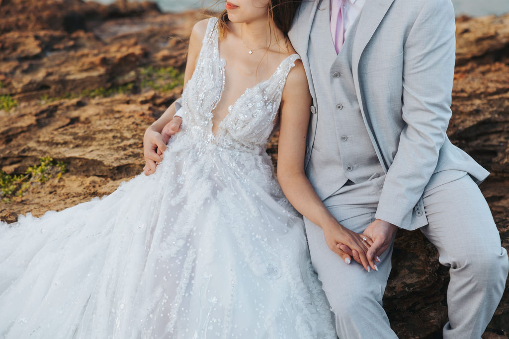 bride and groom sitting on rocky cliff in kauai hawaii