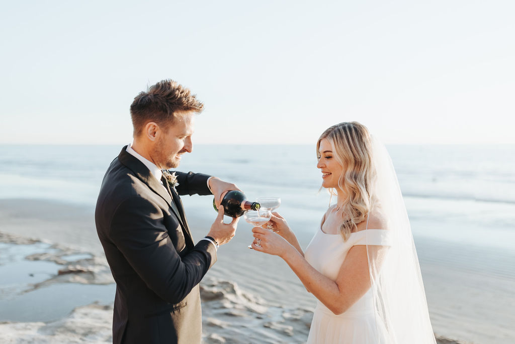 bride and groom drinking champagne on california beach