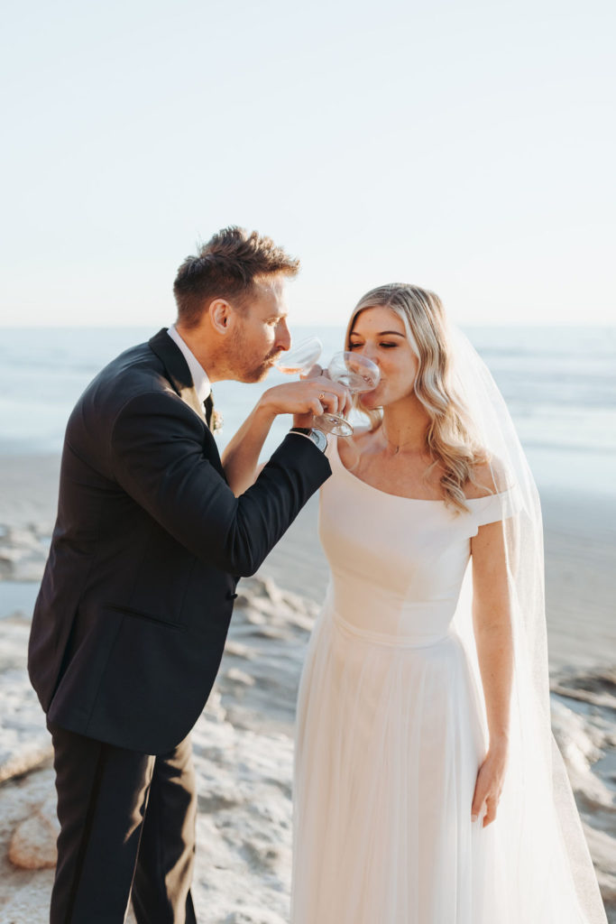 bride and groom drinking champagne on california beach