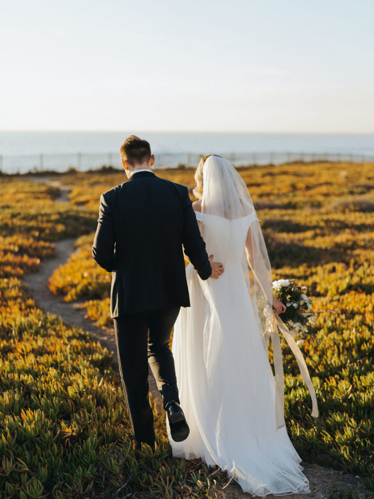 bride and groom walking toward the ocean at sunset in los angeles