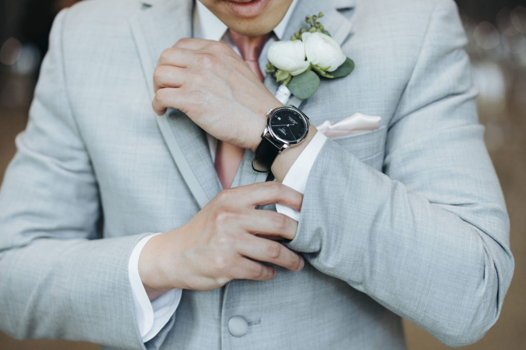 groom wearing gray suit and pink tie with boutonniere and watch