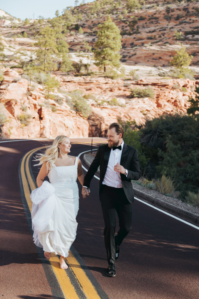 bride and groom walking on road in zion national park