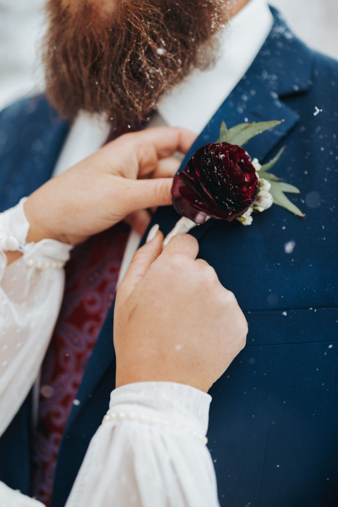 bride adjusting groom's red boutonniere with