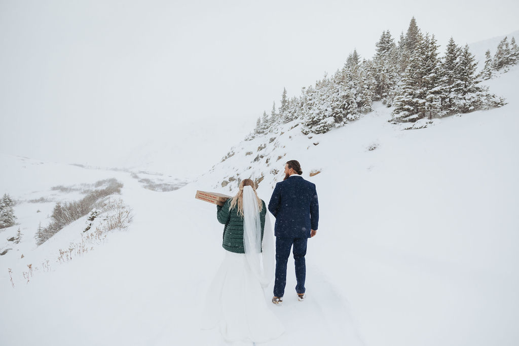bride and groom walking in the snow with pizza