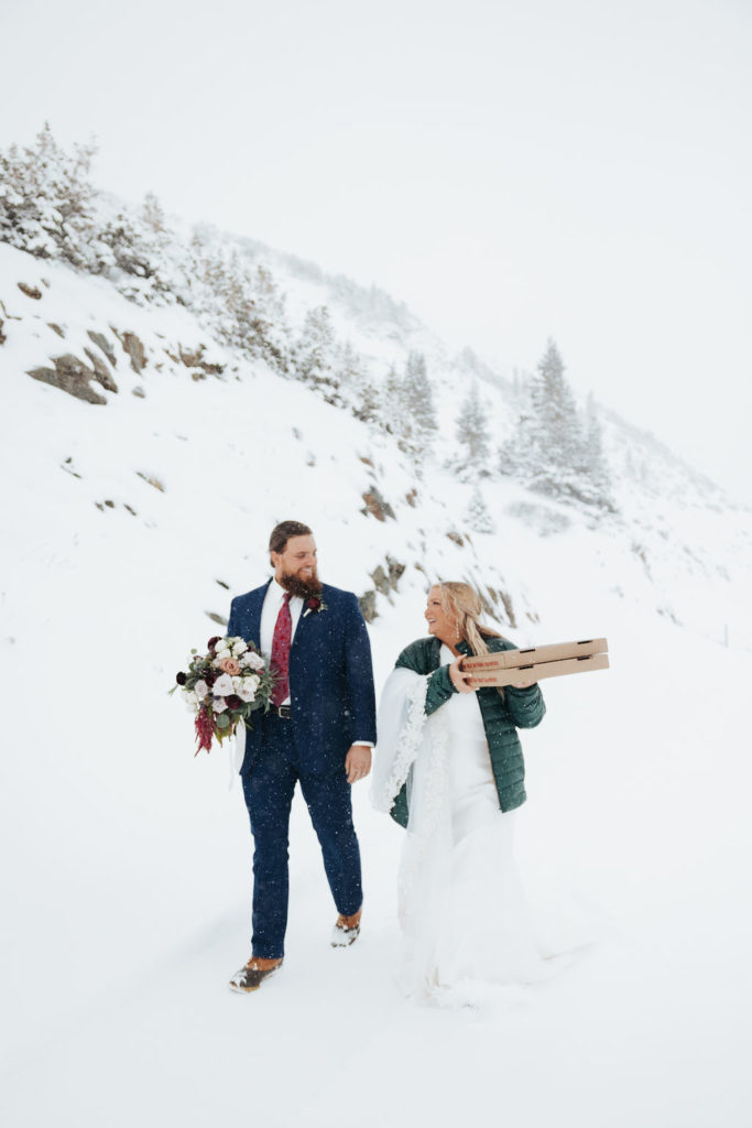 bride and groom walking in the snow with pizza