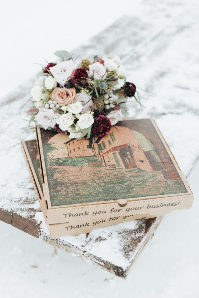 red and pink bridal bouquet on top of pizza box in the snow