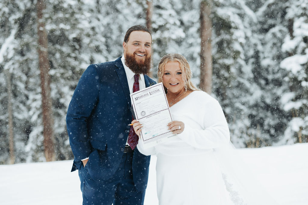Bride and groom holding marriage license snowy mountain elopement