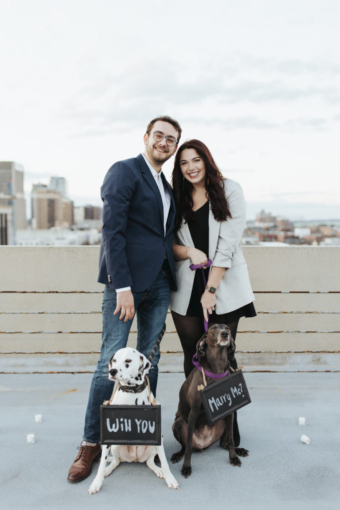engaged couple with two dogs wearing signs for proposal