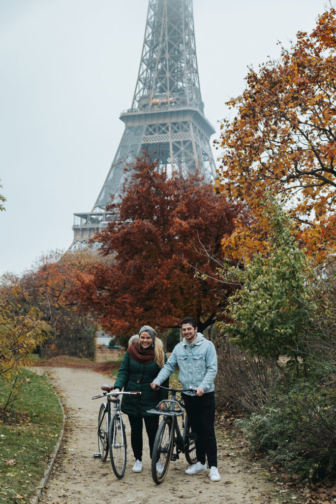 couple holding bikes in front of eiffel tower and fall trees