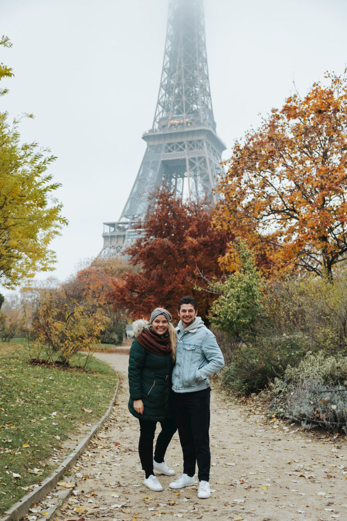 couple standing in front of eiffel tower surrounded by fall colors