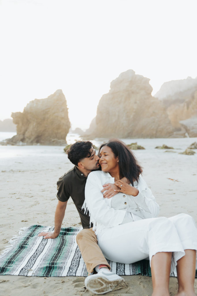engaged couple sitting on a blanket at the beach