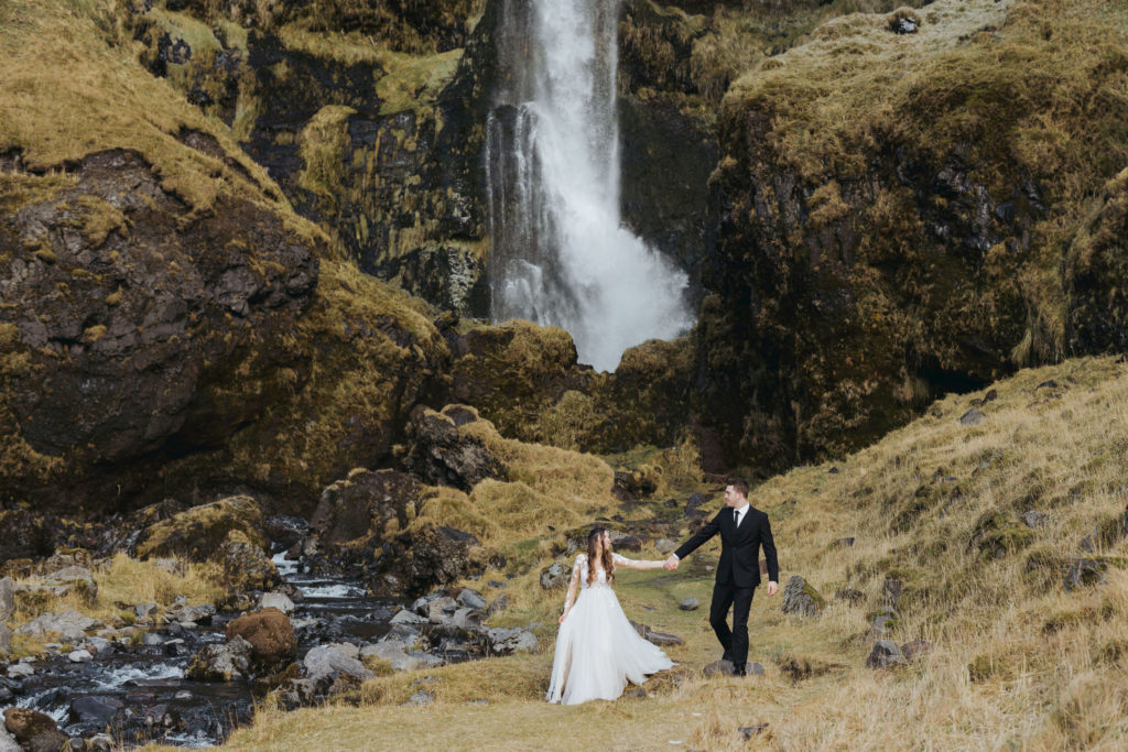bride and groom holding hands iceland elopement ceremony with waterfall and mountains