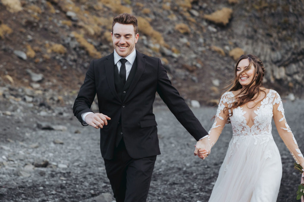 bride and groom holding hands on black sand beach in iceland