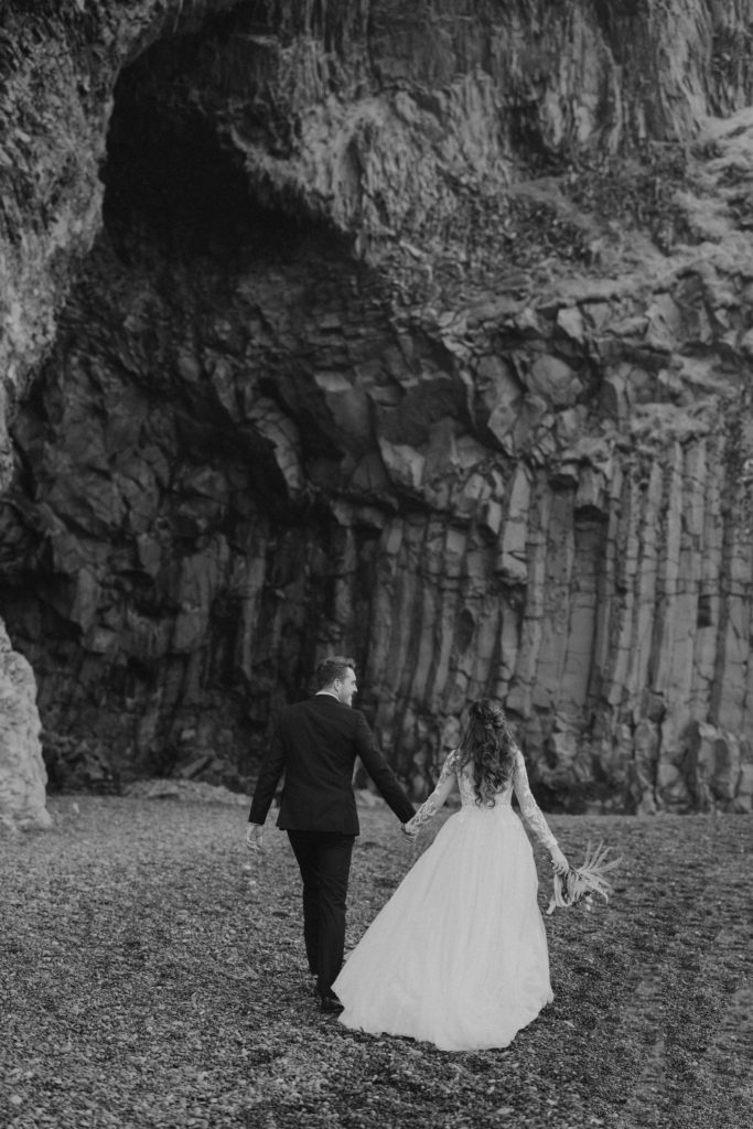 bride and groom holding hands on black sand beach in iceland