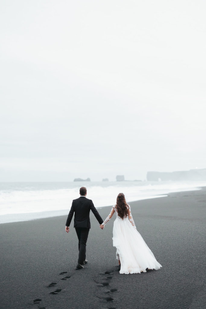 bride and groom walking on black sand beach iceland