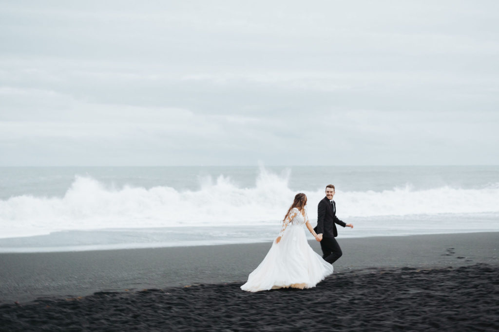 bride and groom running on black sand beach iceland