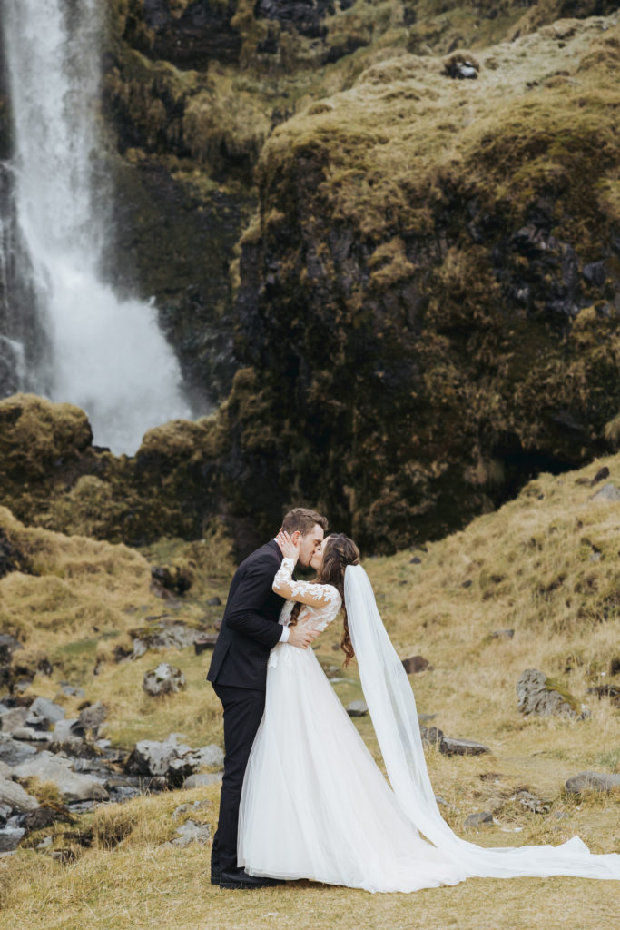 Groom kissing bride iceland elopement ceremony with waterfall and mountains