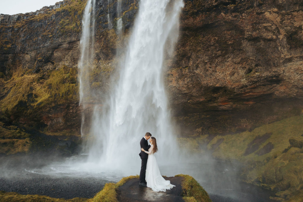 bride and groom elopement walking under waterfall in iceland