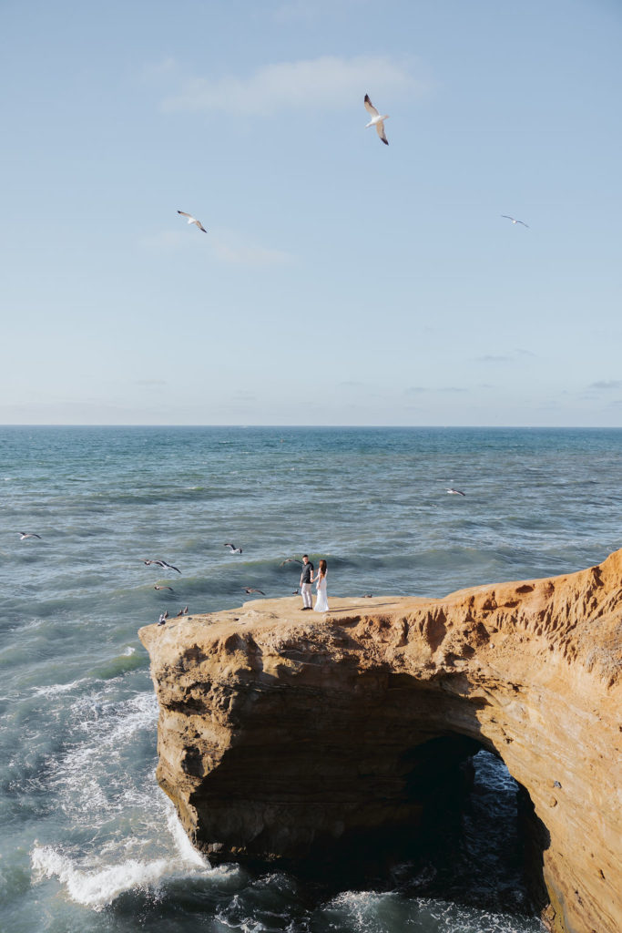 engaged couple holding hands and walking on san diego cliffs