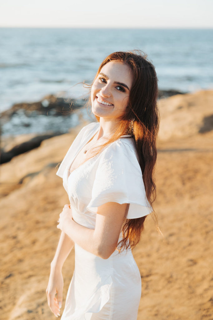 woman in white flutter sleeve dress standing on san diego cliffs at sunset