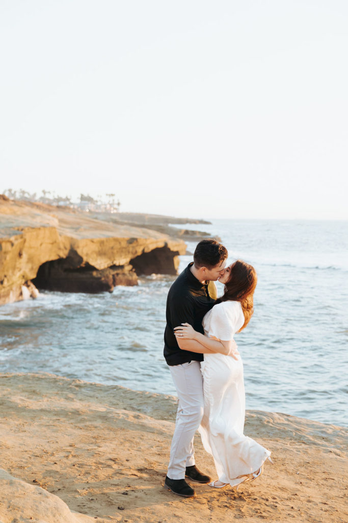 engaged couple kissing on san diego coast with ocean in the background