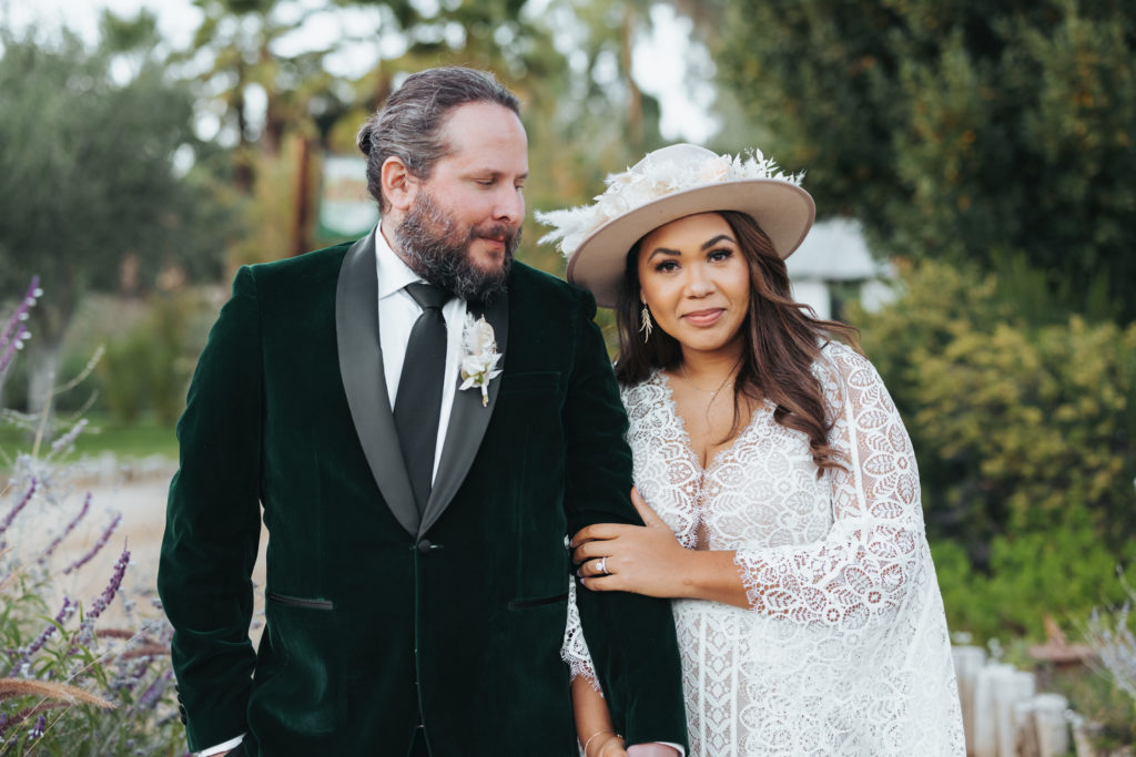 bride wearing white floral hat with groom wearing green velvet suit
