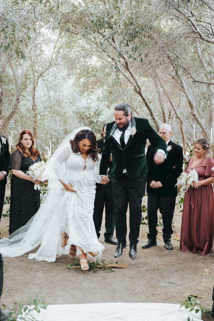 bride and groom jumping over broom in wedding ceremony