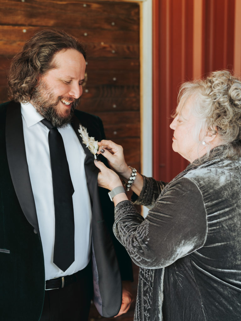 mother attaching groom's boutonniere to coat