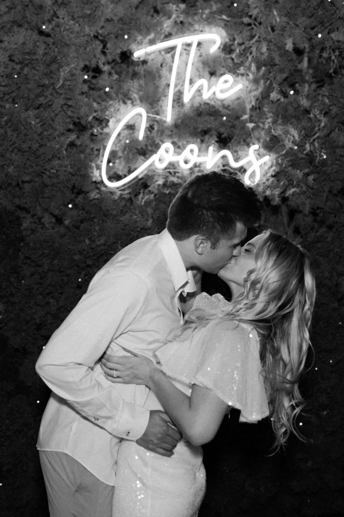 bride and groom first kiss with neon sign