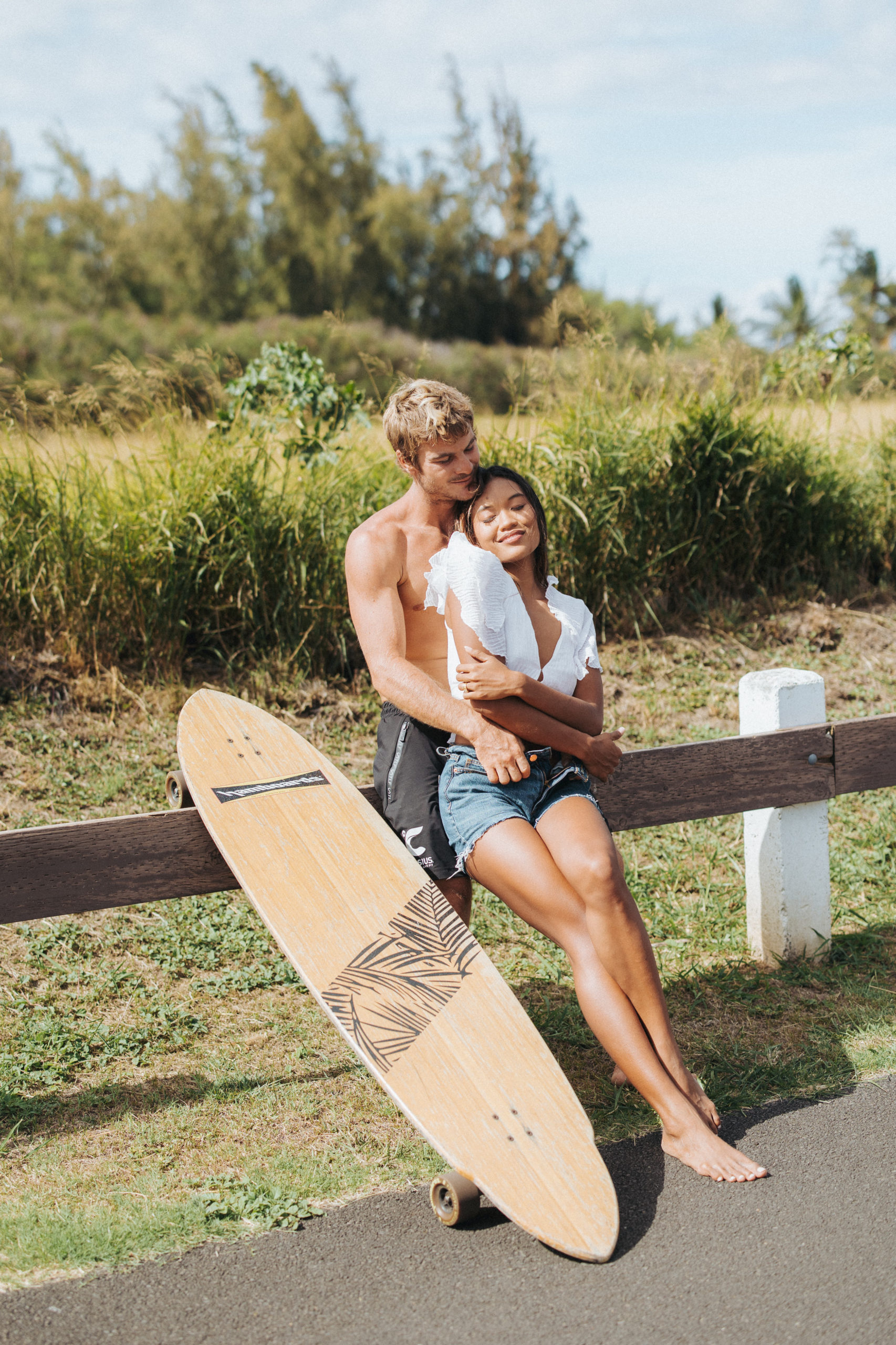couple leaning on a fence with a longboard