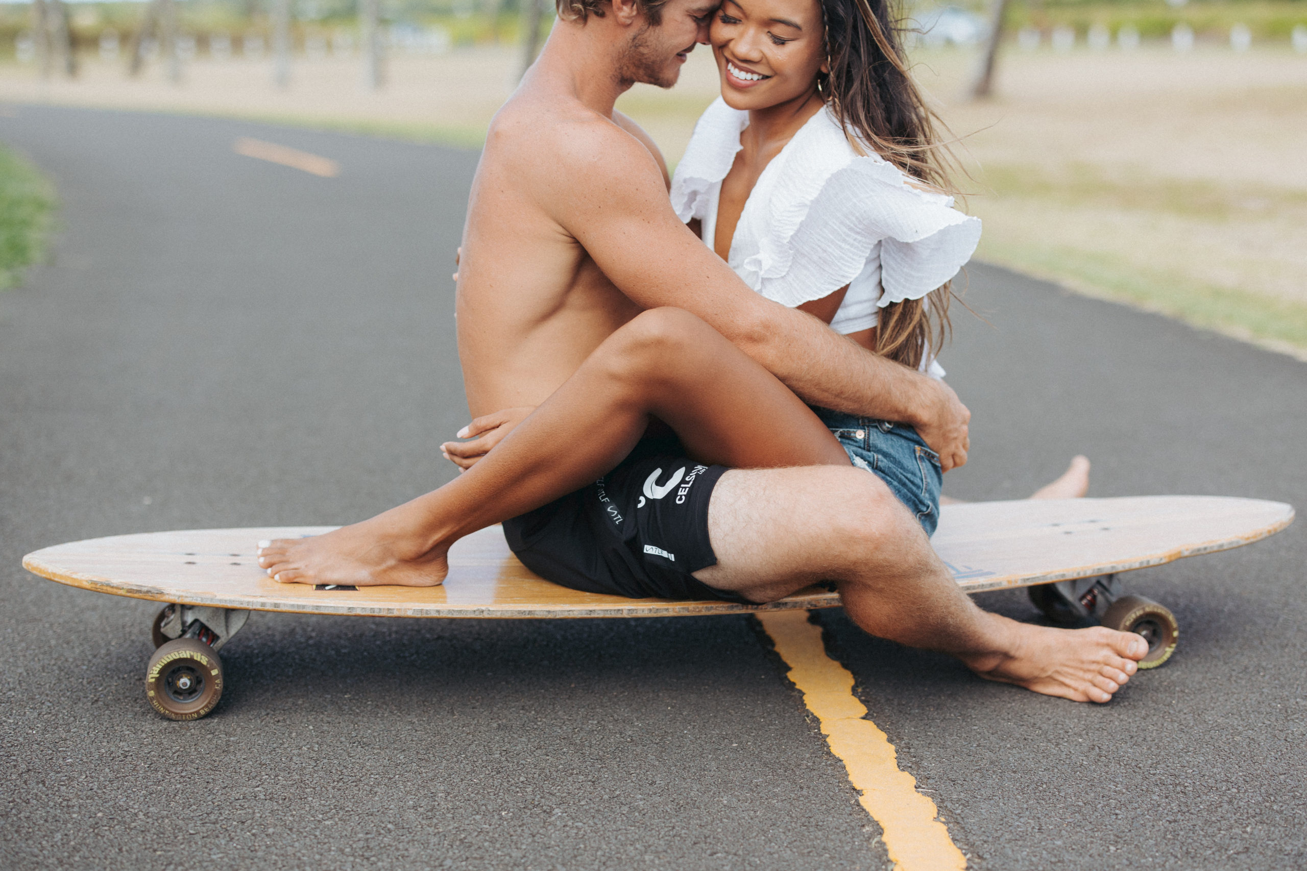 couple hugging on a longboard with palm trees