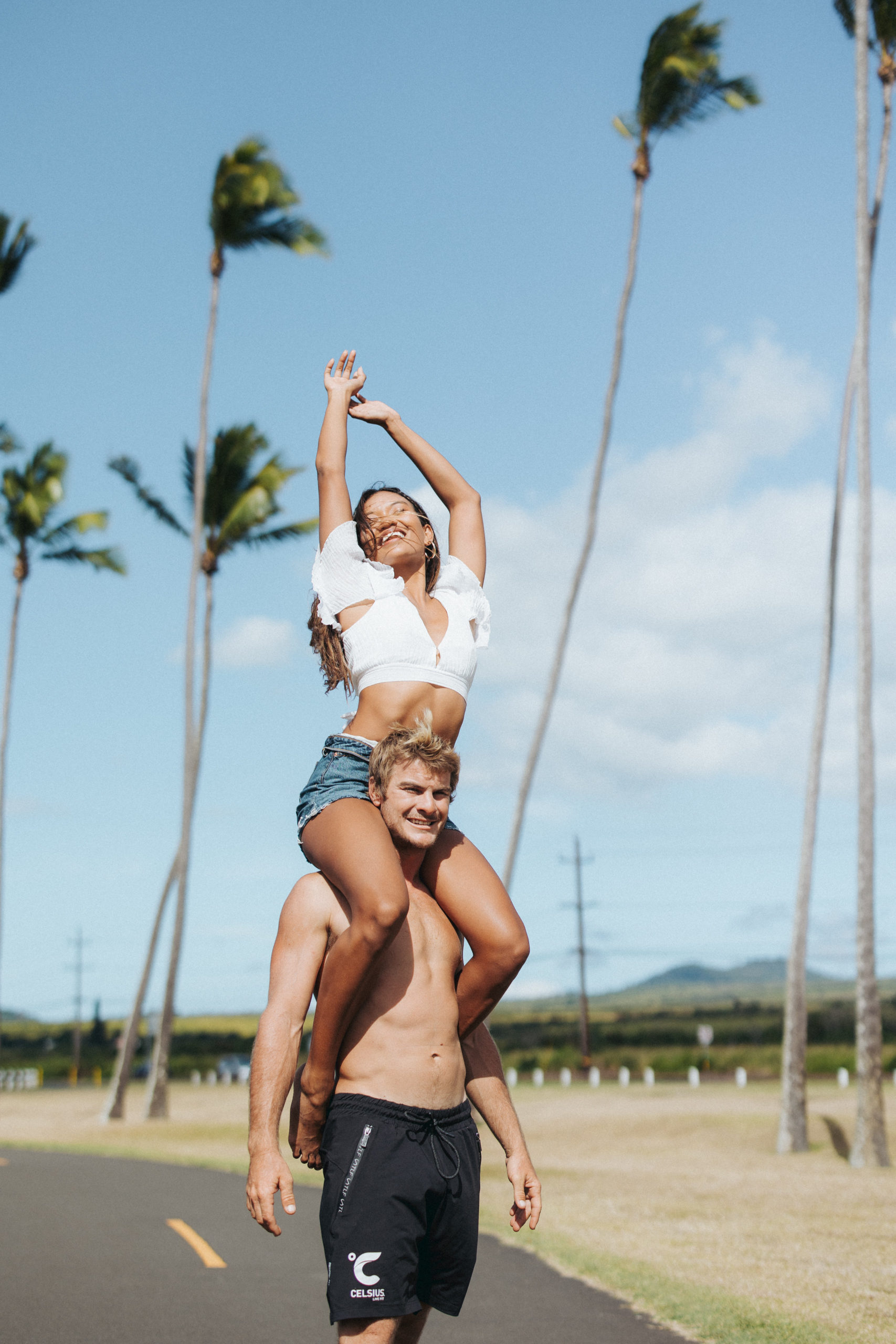 woman on top of man's shoulders in front of palm trees