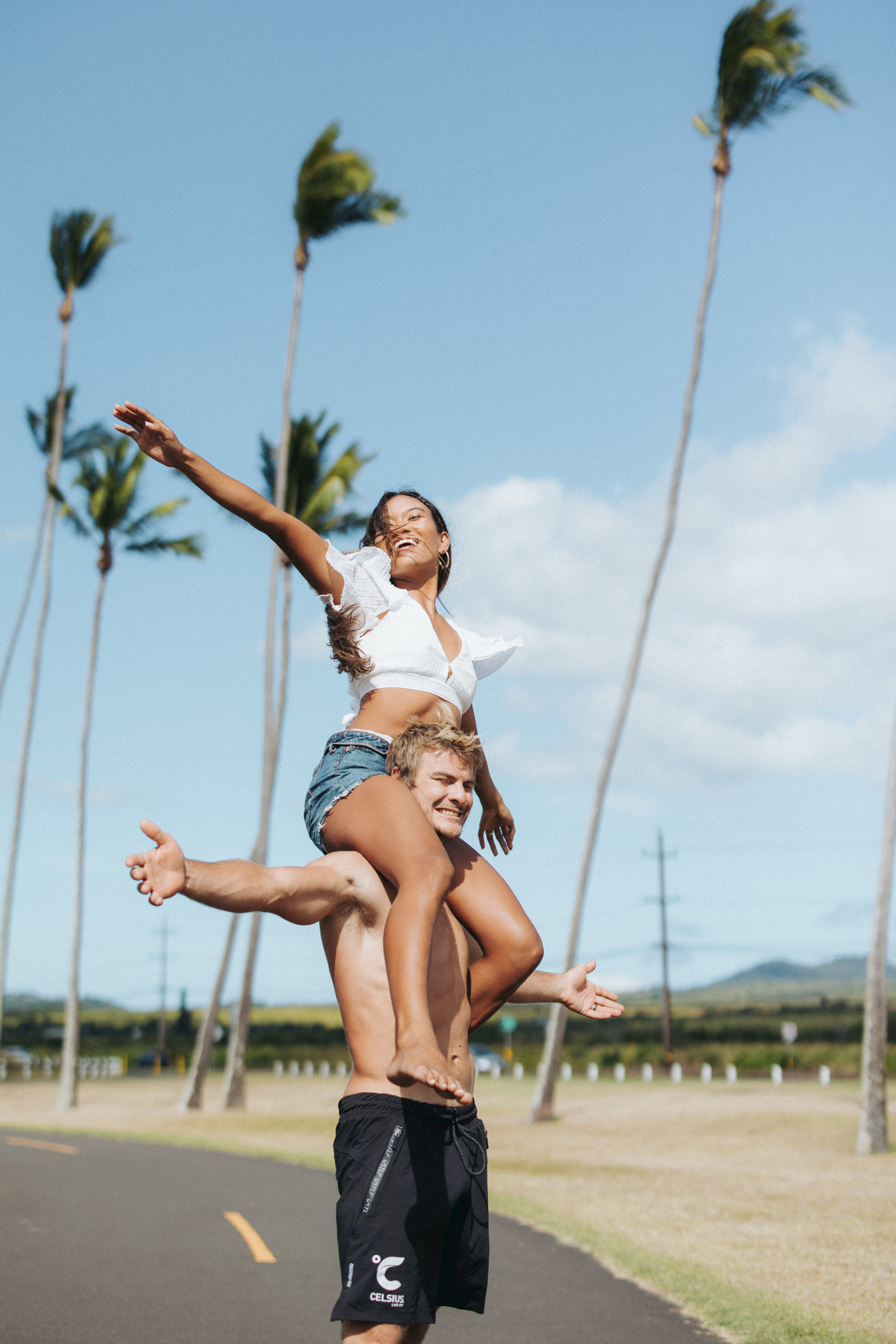woman on top of man's shoulders in front of palm trees