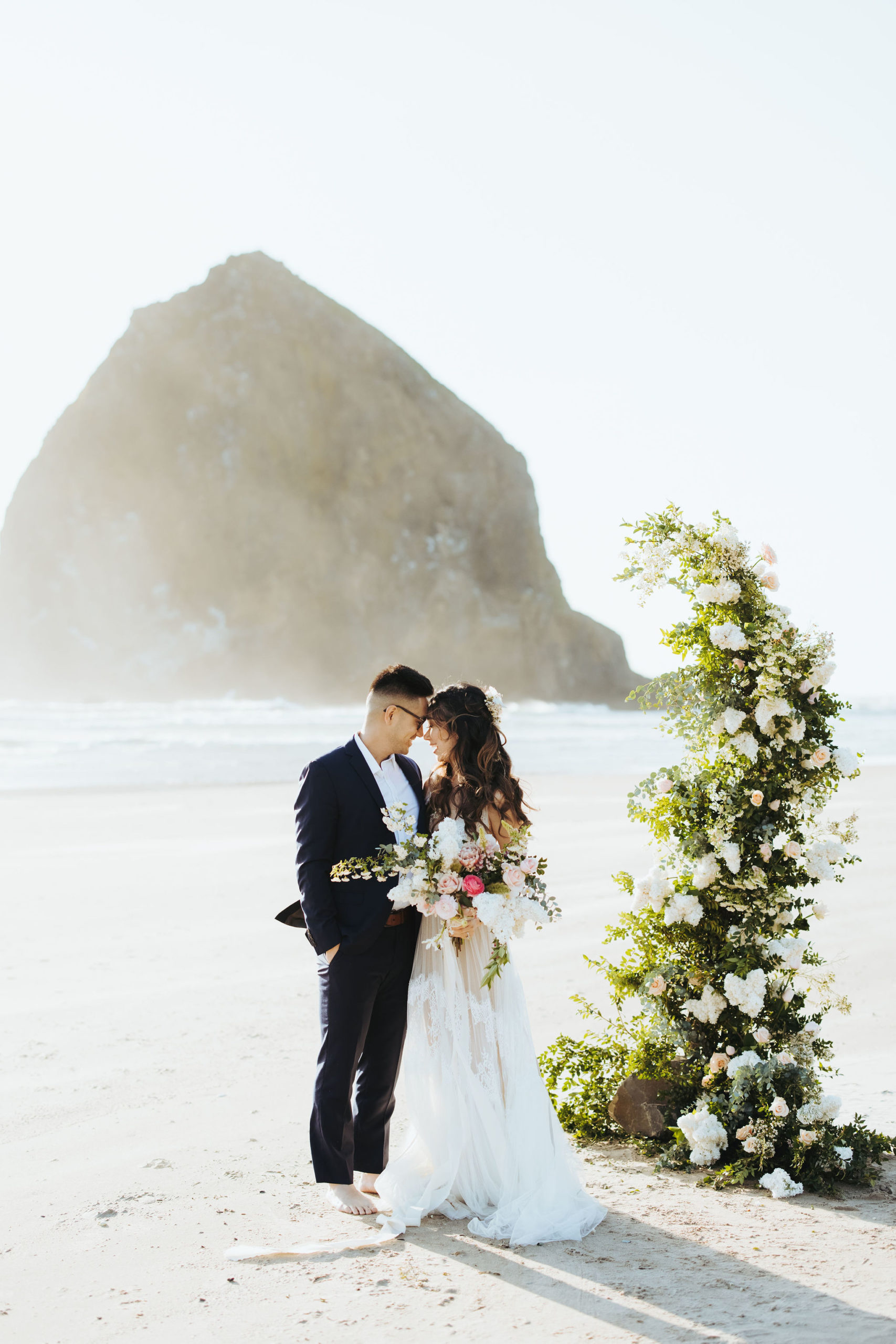 bride and groom elopement portraits on beach with flower arch and candles