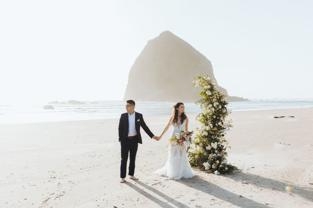 bride and groom elopement portraits on Oregon Coast beach with flower arch and candles