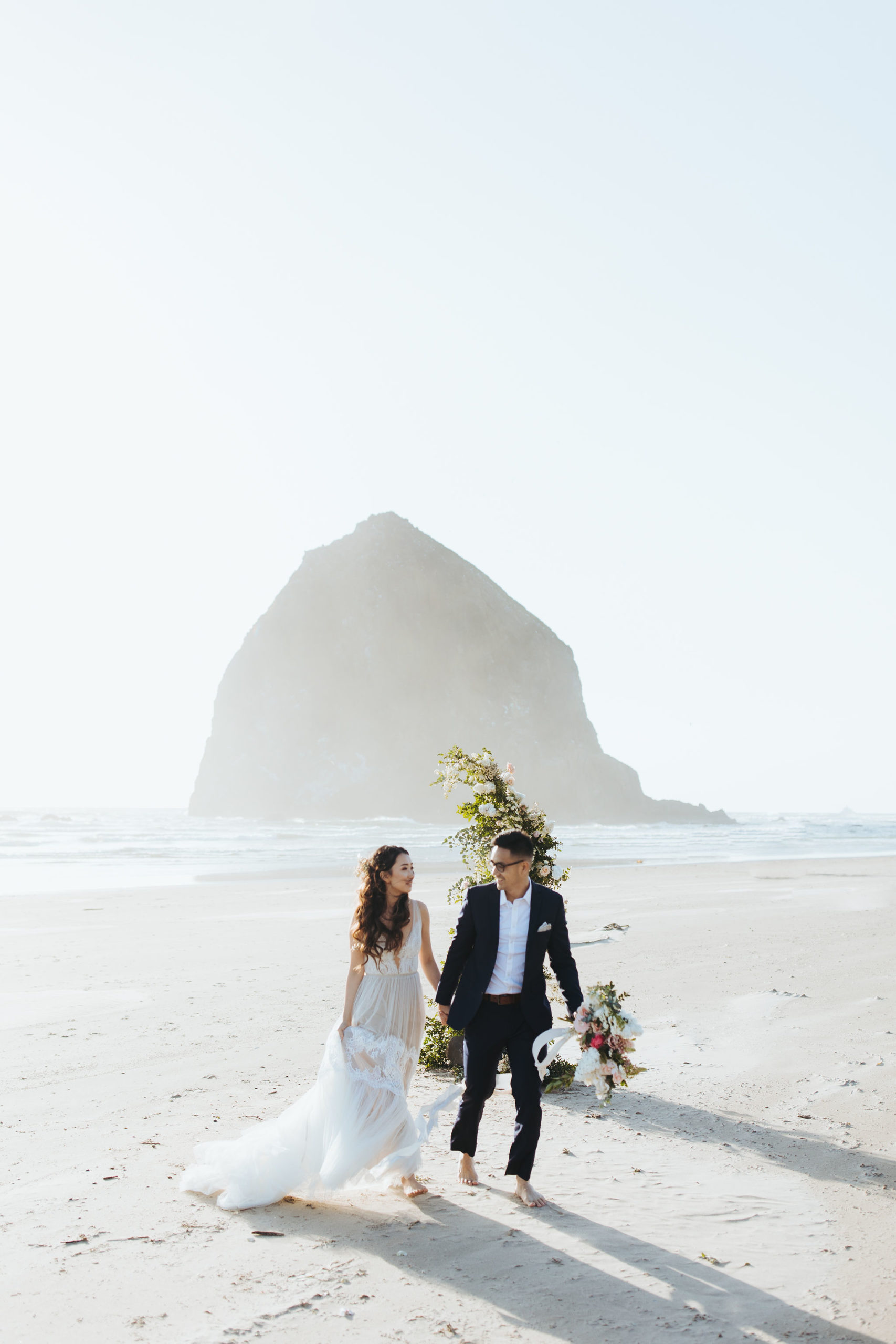 bride and groom portrait on Oregon Coast  beach with flower arch and candles