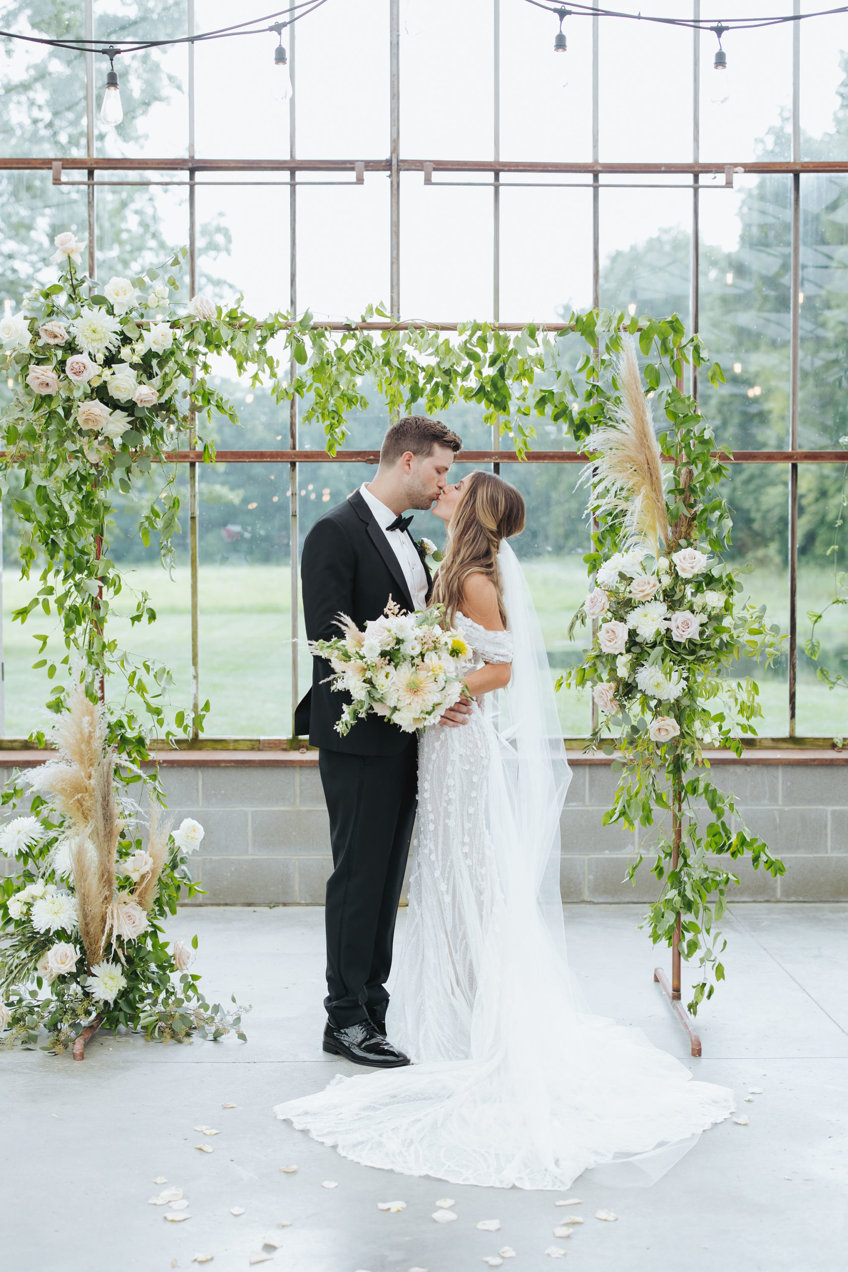 bride and groom kissing under floral arch