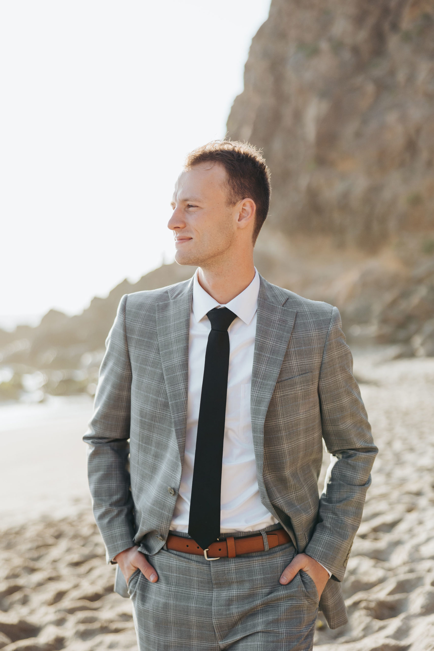 groom posing in front of rocky cliff on the beach at Point Dume