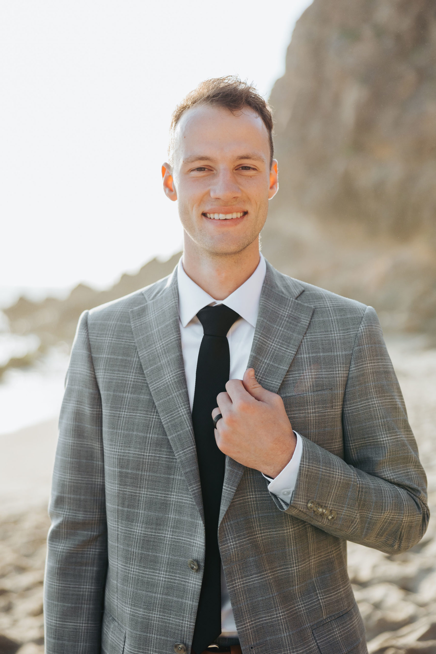 groom posing in front of rocky cliff on the beach