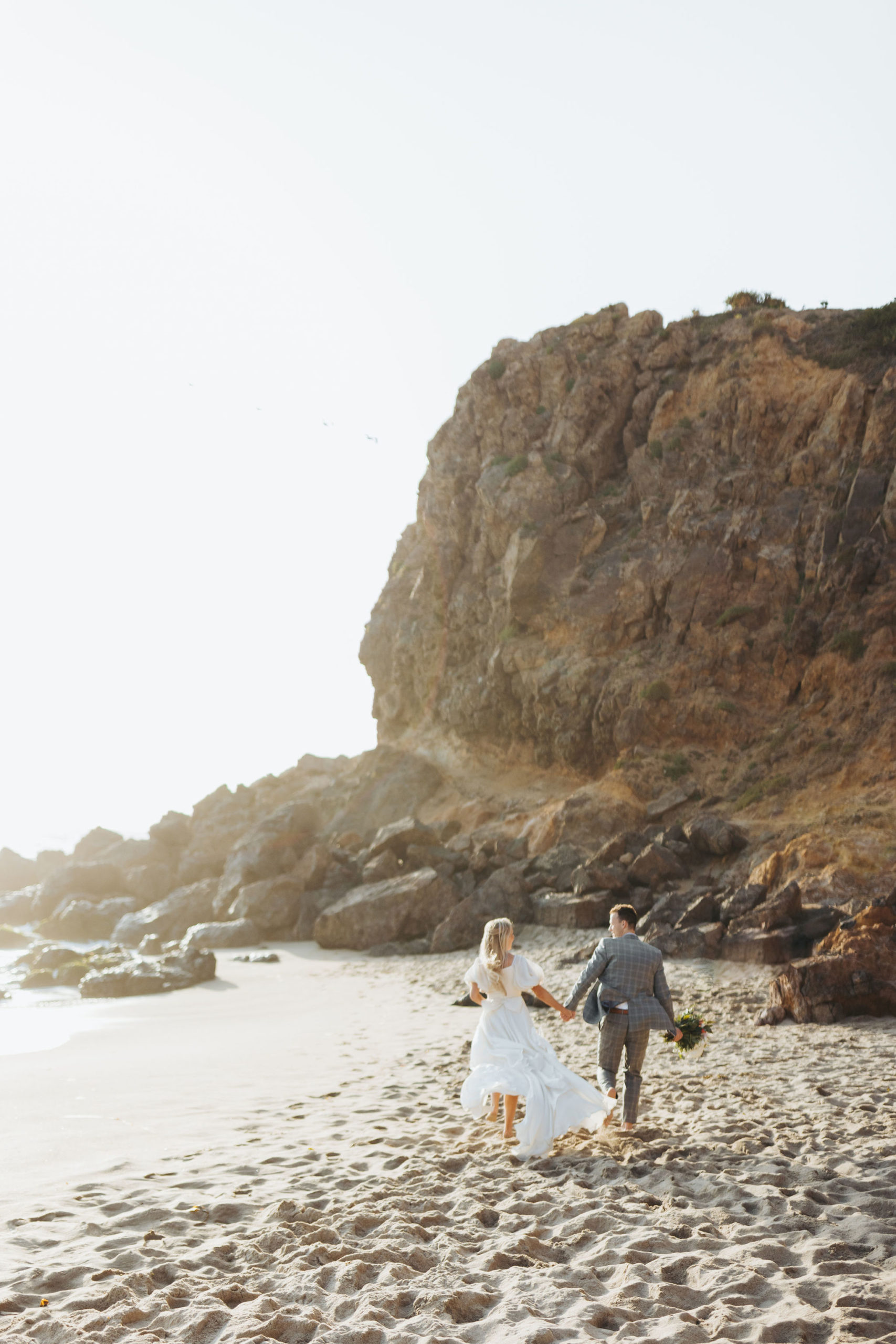 bride and groom holding hands walking on a beach at Point Dume